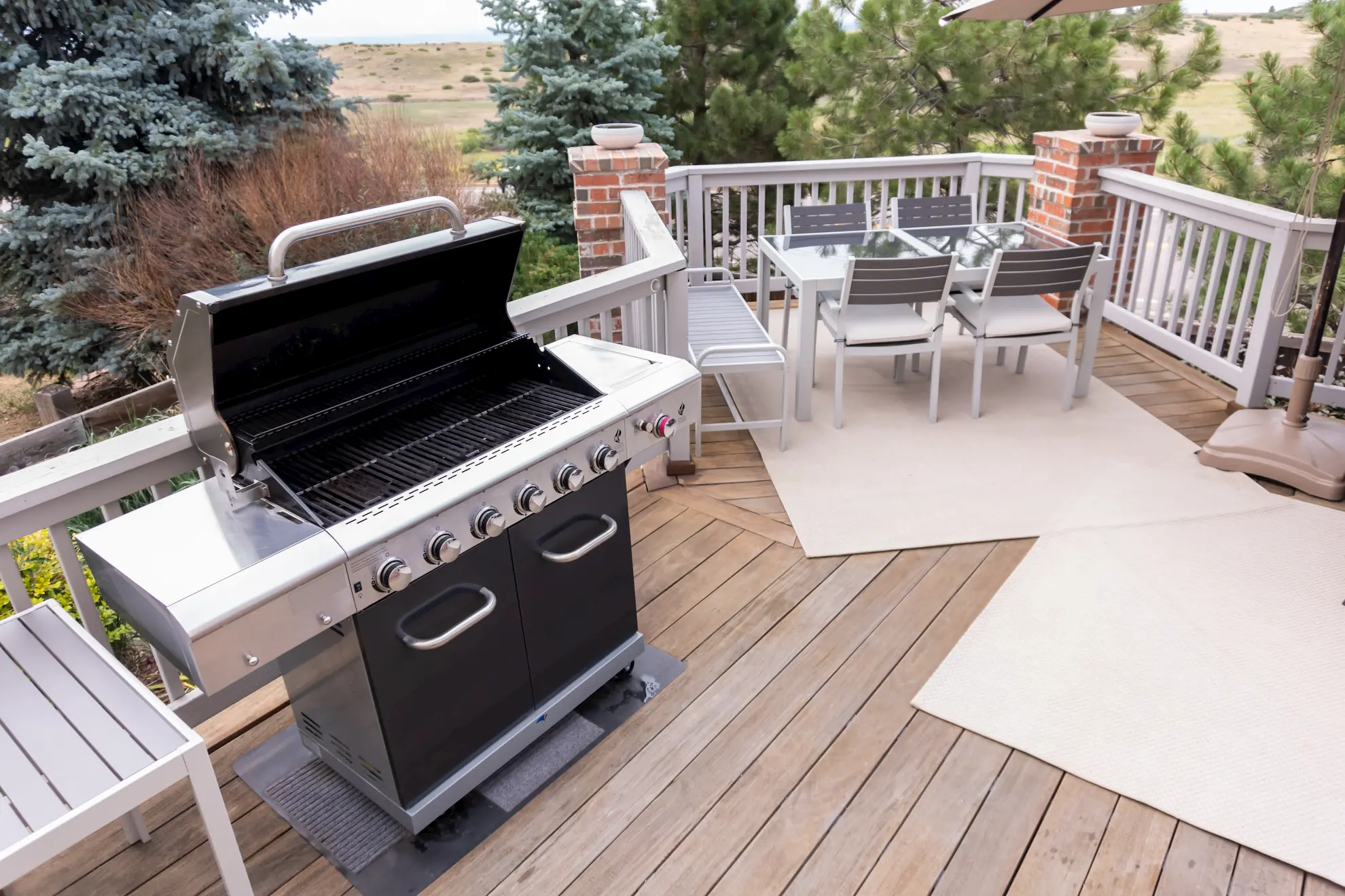 Black gas grill on wooden deck with dining table and chairs in the background