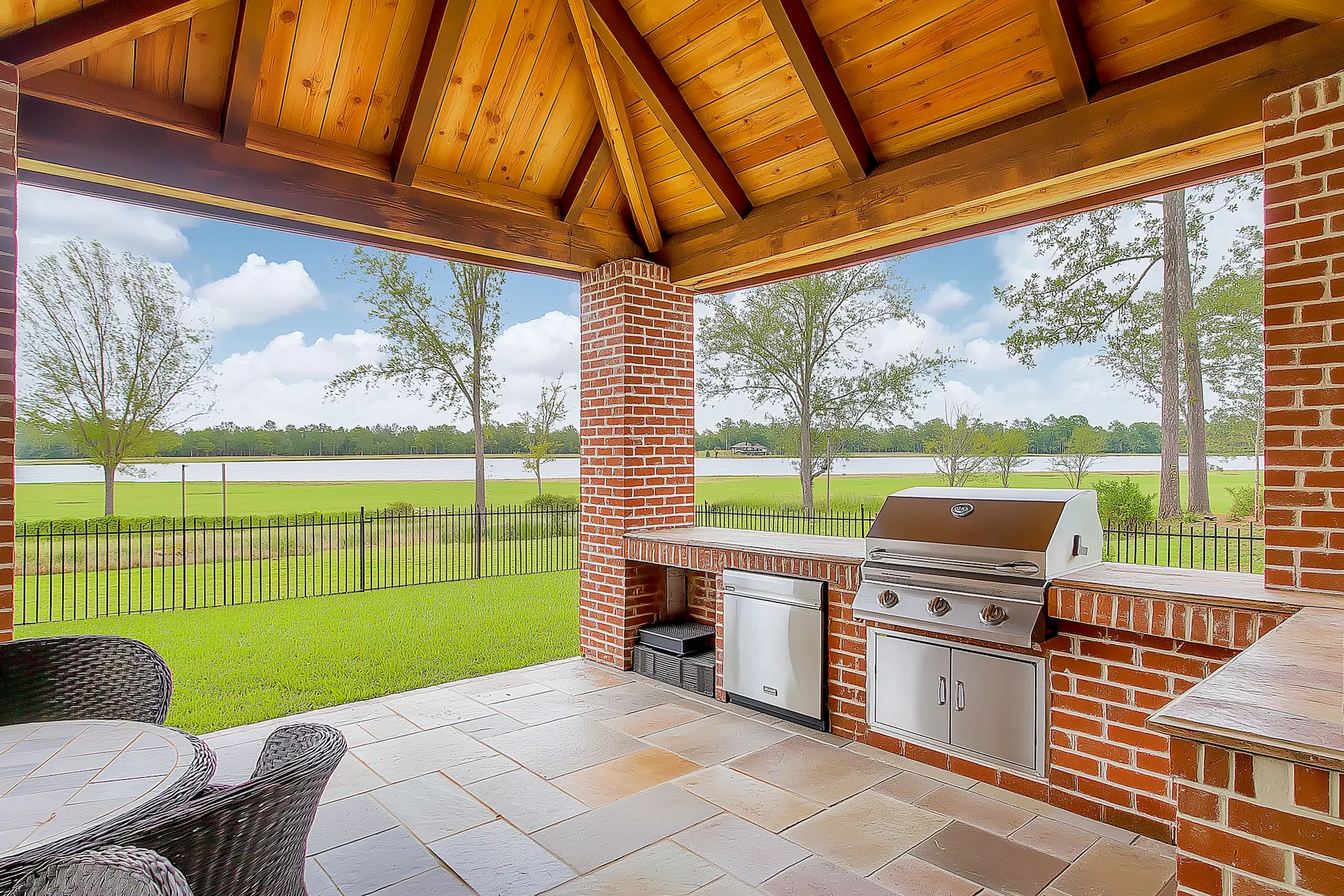 Covered outdoor kitchen with stainless steel grill and views of the lake through trees