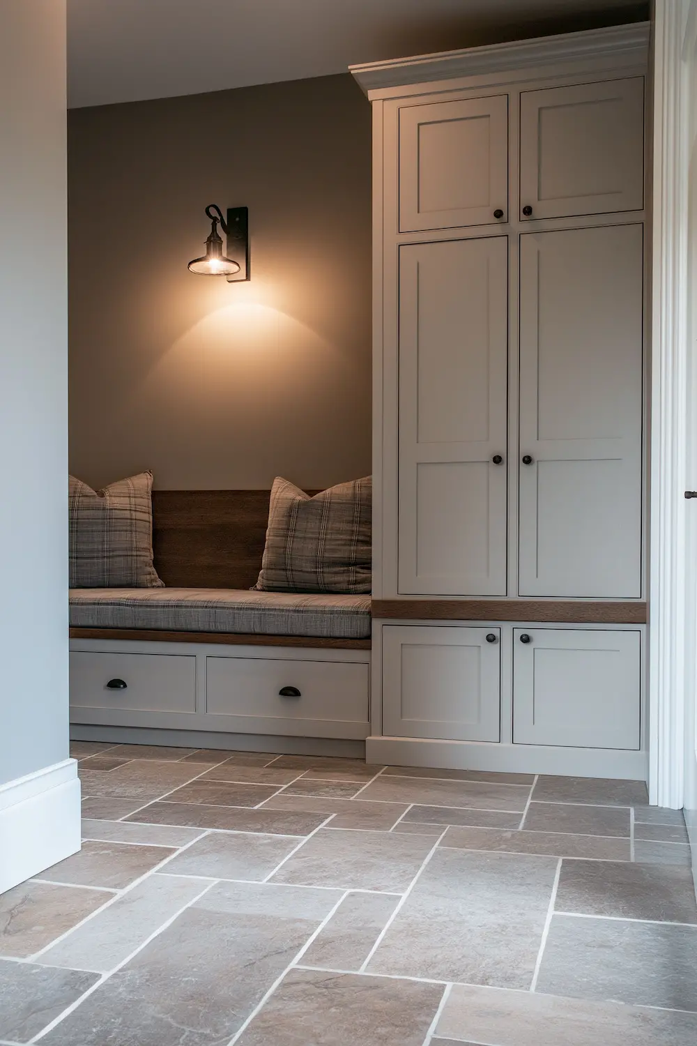 Cozy mudroom with a bench seat and storage cabinets illuminated by a wall sconce, stone flooring