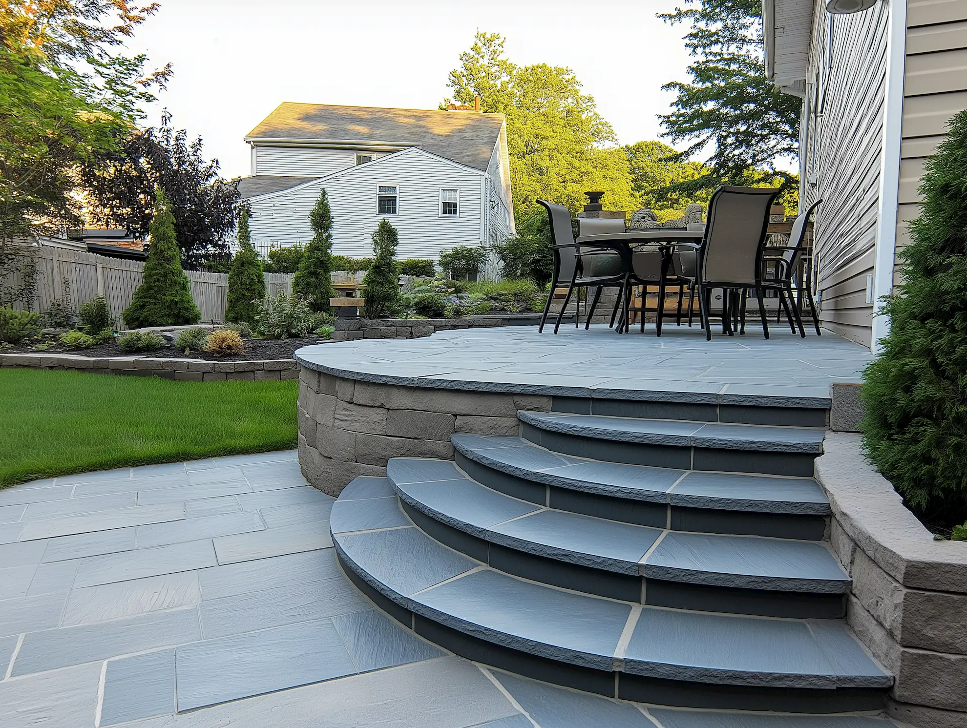 Curved stone steps leading to a patio with outdoor dining furniture and lush landscaping