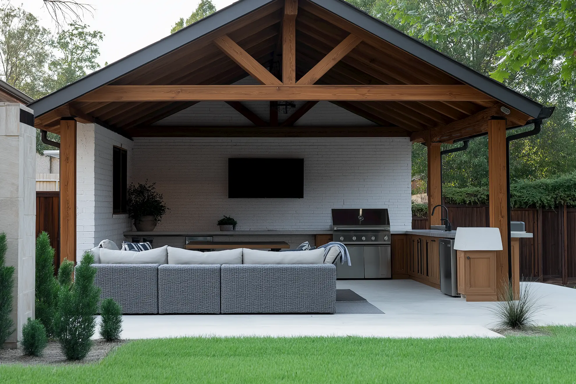 Modern outdoor kitchen, lounge with gray sofa stainless steel grill and TV under wooden gazebo