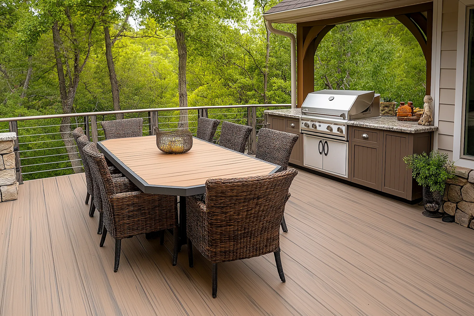 Outdoor dining area with a grill surrounded by greenery and wicker chairs on a deck porch