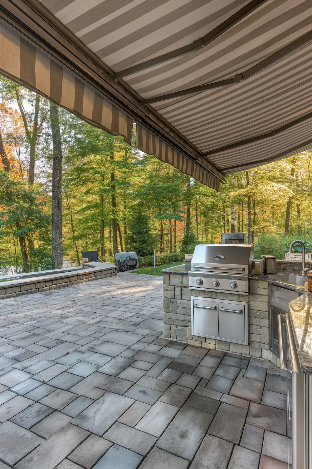 Outdoor kitchen with a grill under a striped awning surrounded by colorful autumn trees