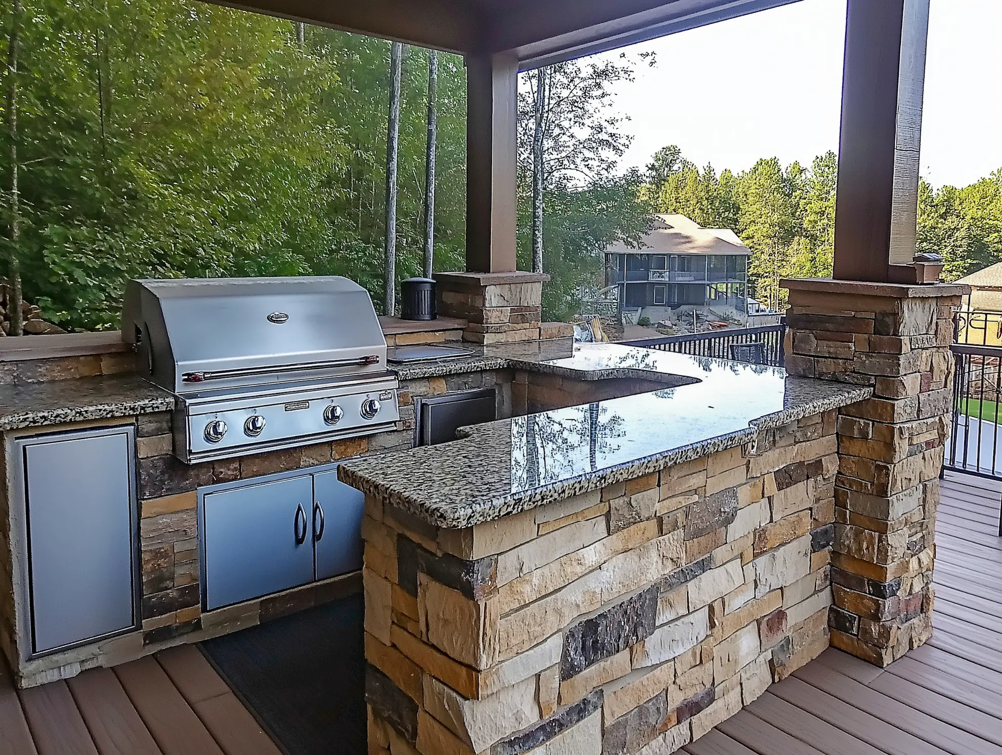 Outdoor kitchen with granite countertop and stainless steel grill surrounded by trees