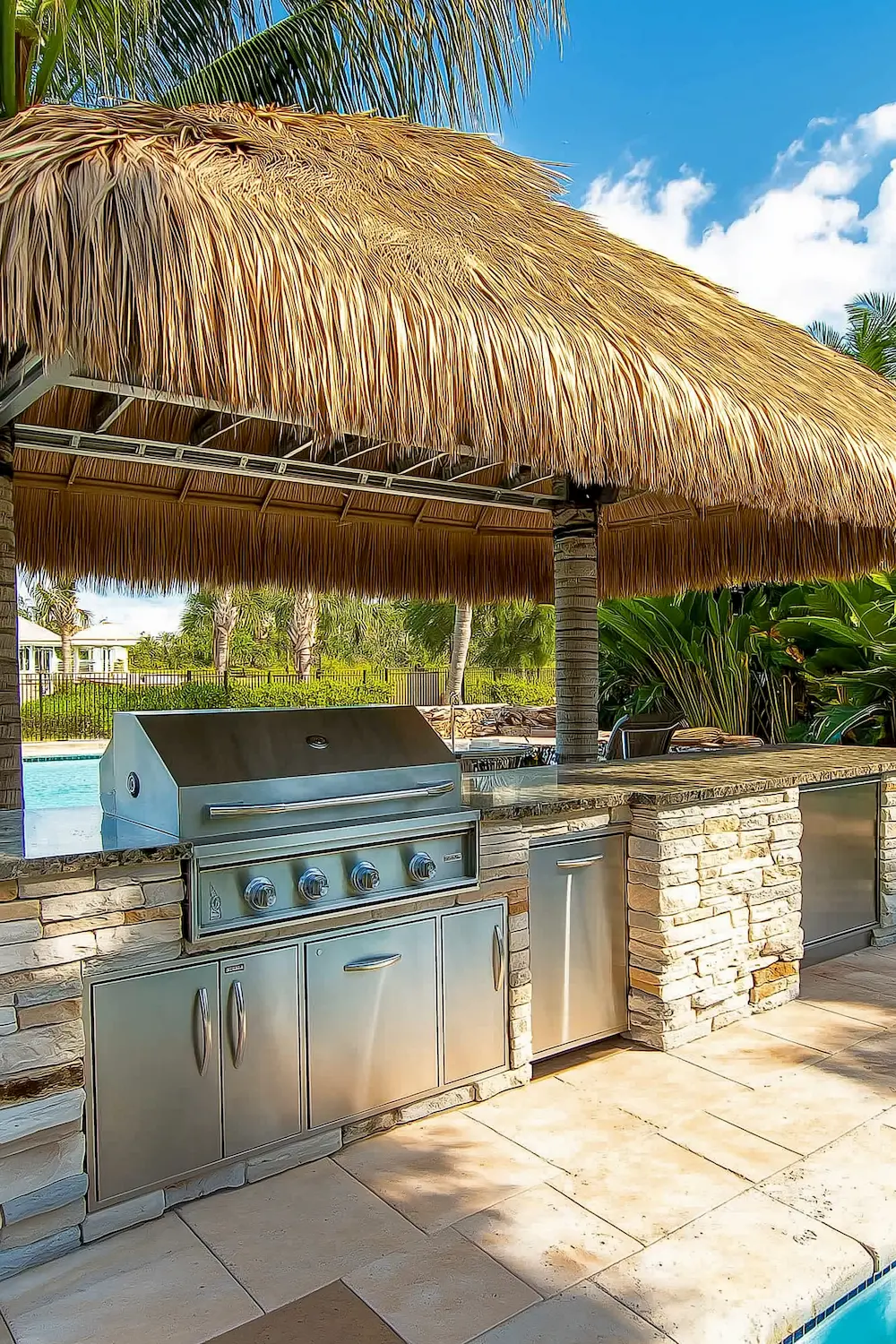 Outdoor kitchen with stainless steel grill and stone countertop under thatched roof - Tropical Outdoor Kitchen with Tiki Bar