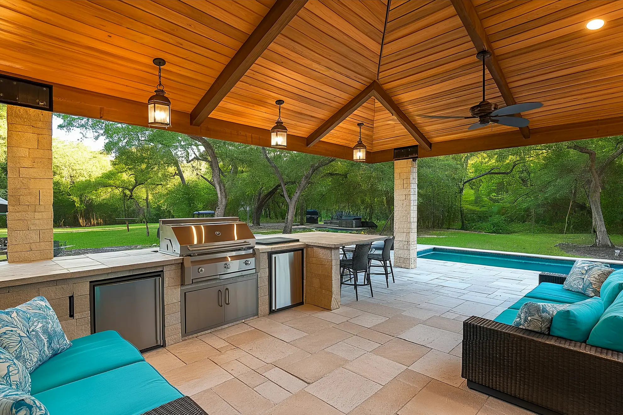 Outdoor kitchen with stainless steel grill seating area and pool in a lush green yard