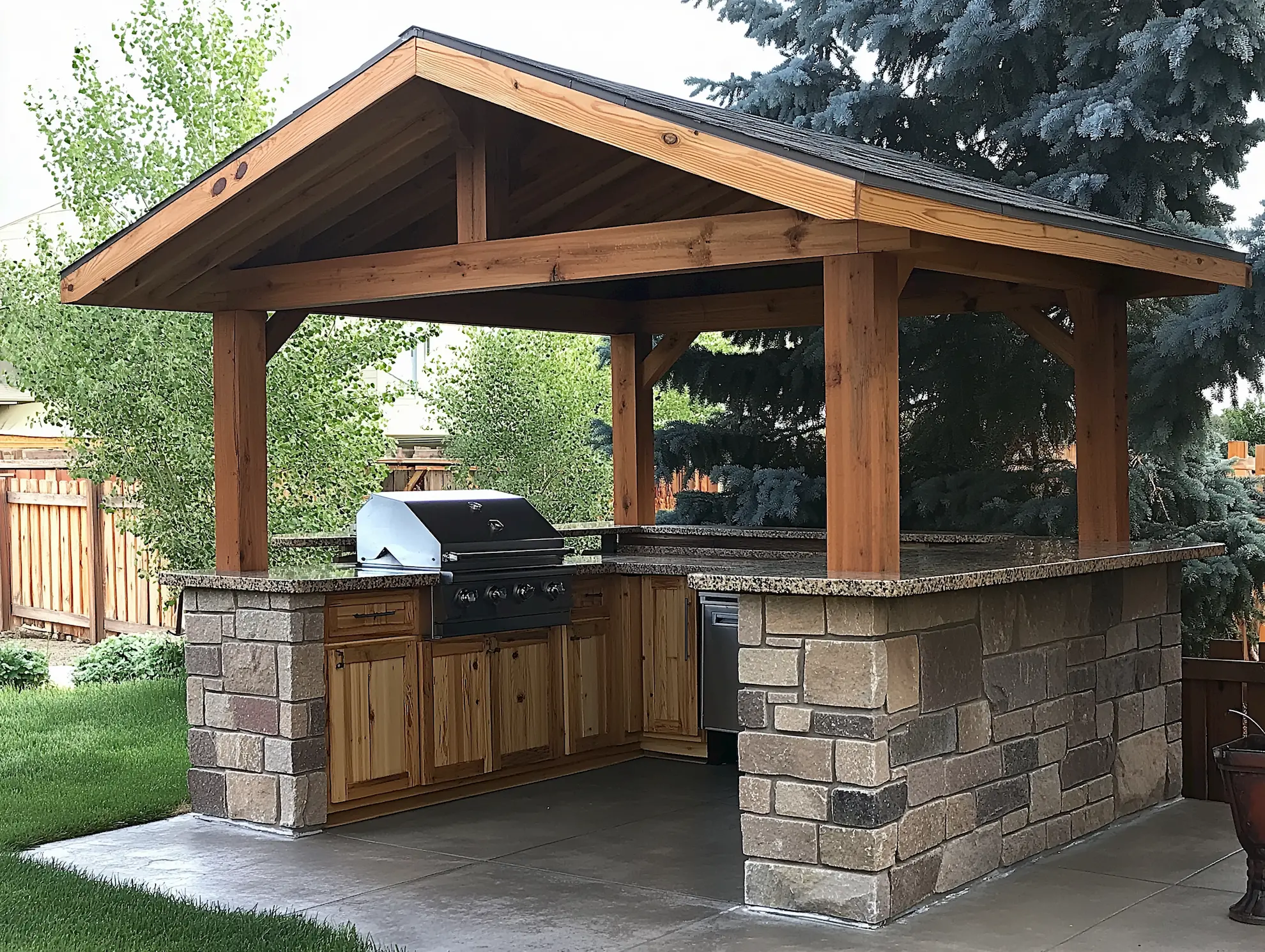 Pavilion outdoor kitchen with stone countertop and gas grill surrounded by greenery