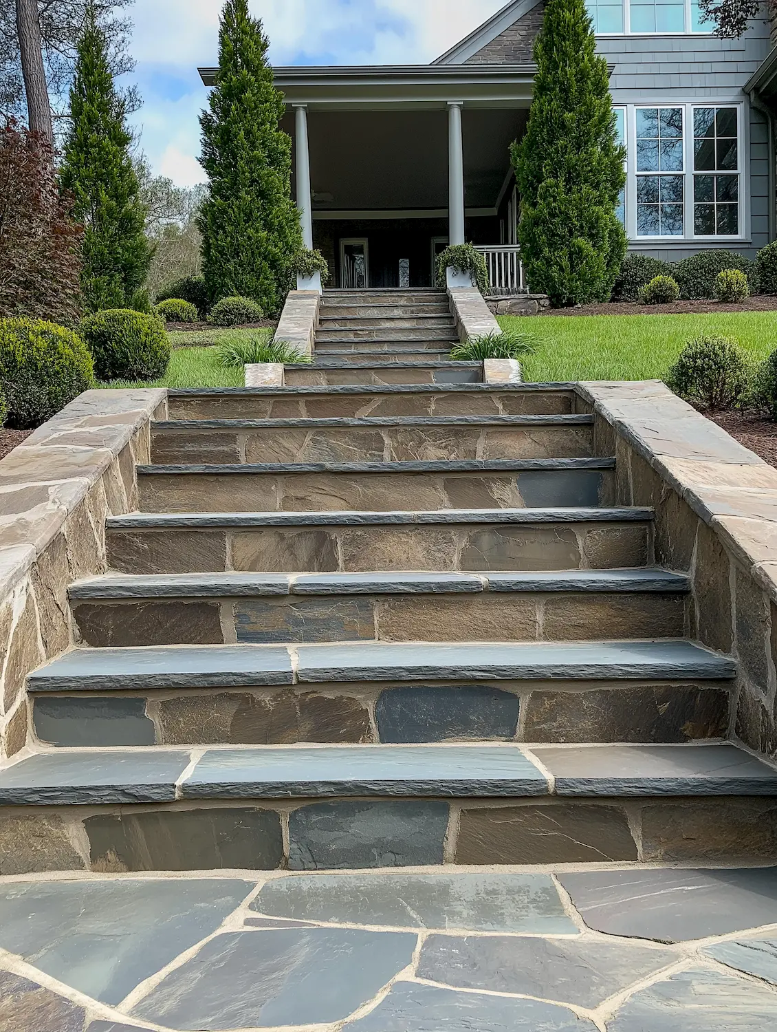 Stone staircase leading to a house with well-maintained landscaping and greenery