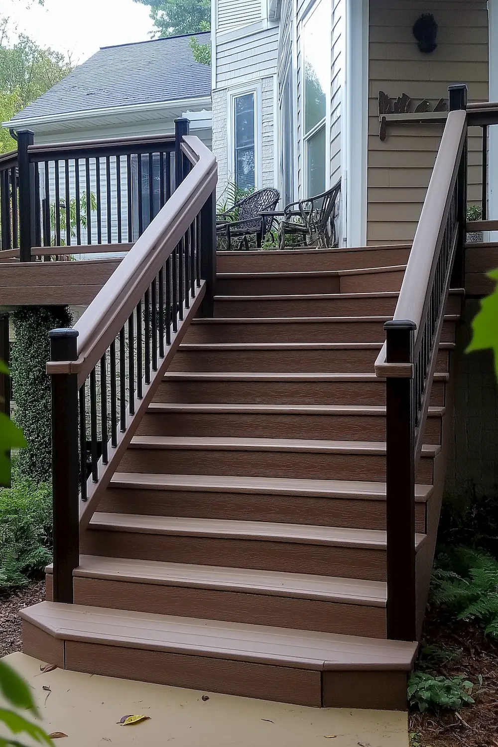 Sturdy brown stairway leading to a house with a black railing and seating area visible