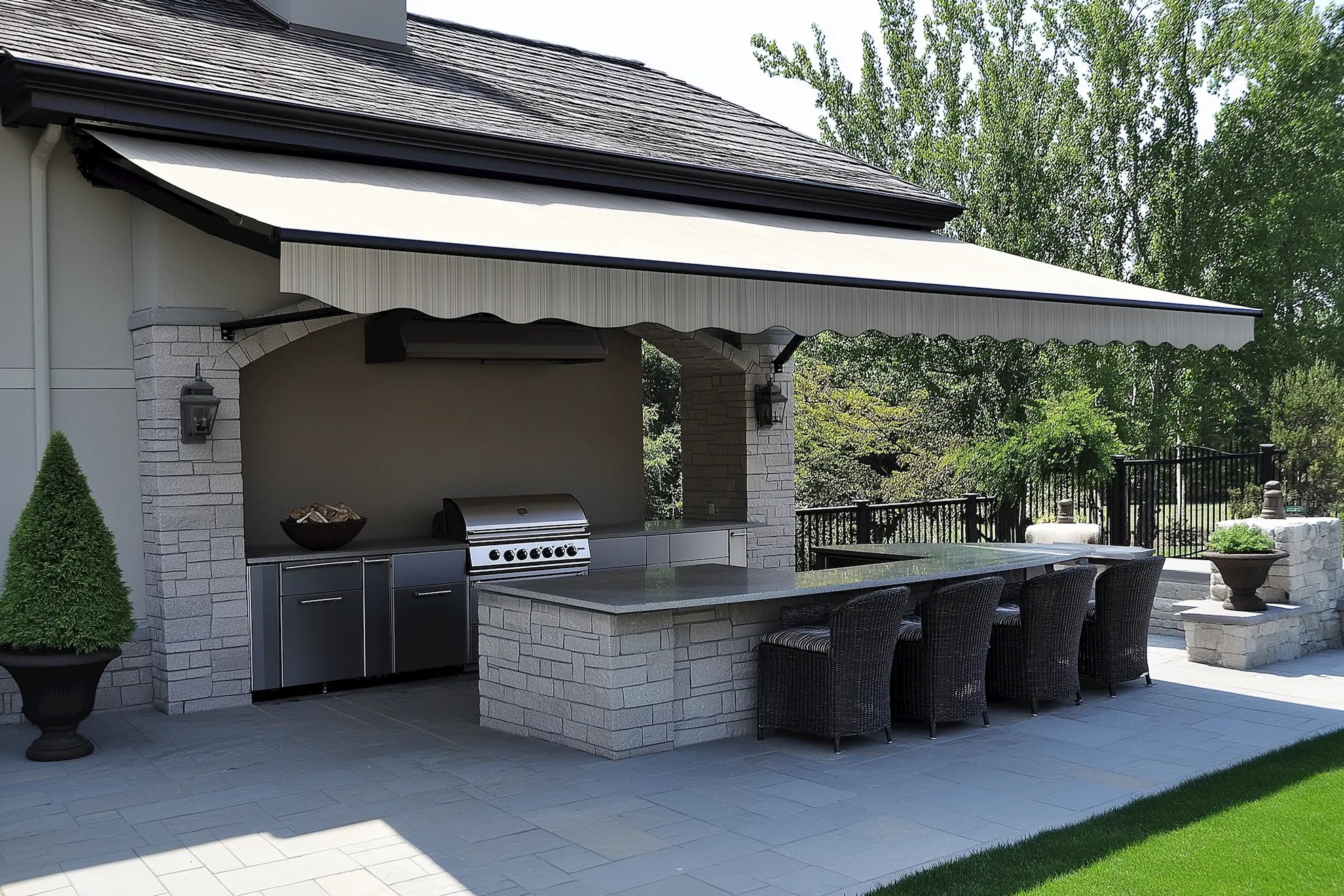 outdoor kitchen with grill and seating under an awning surrounded by greenery and awnings opened