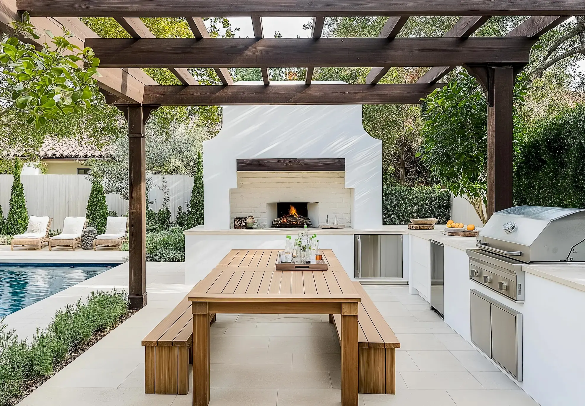 outdoor-kitchen-with-wooden-dining-table-and-grill-near-a-pool-and-fireplace